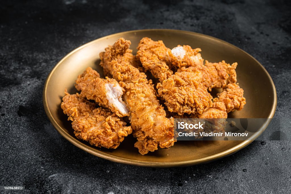 Breaded chicken strips, breast fillet meat on a plate. Black backgrund. Top view.
