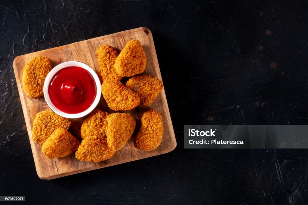 Chicken nuggets with ketchup on a dark background, shot from the top. A crispy meat snack at a restaurant, a fast food dish, with copy space
