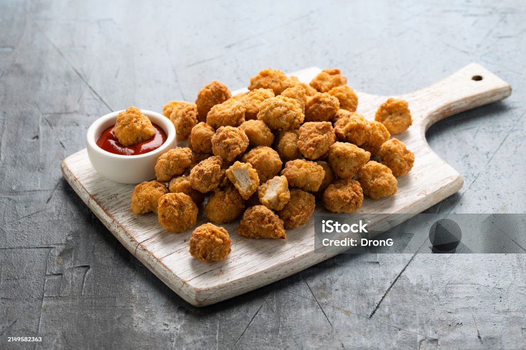 Crispy Popcorn Chicken with ketchup sauce on white wooden board.