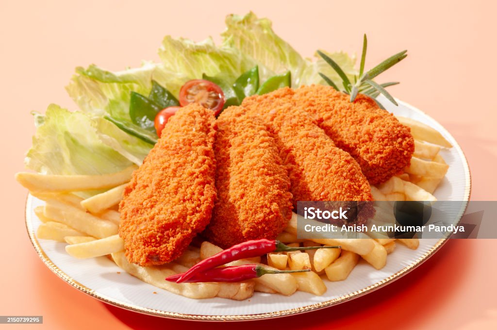 Fried chicken fillets with french fries and salad on an orange background