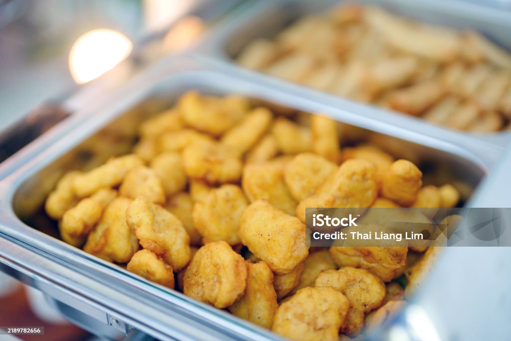 Buffet meal served with a large tray of crispy golden fried chicken nuggets on a serving dish, perfect for catering events and gatherings. The background shows more dishes in a buffet setting.