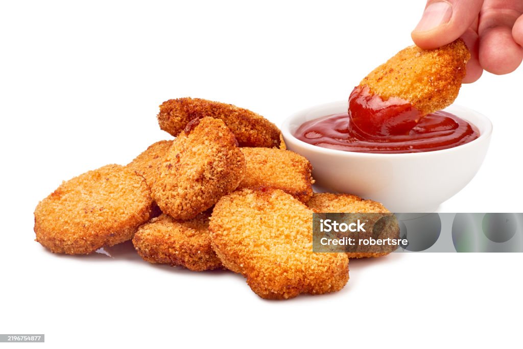 The individual is dunking a piece of deepfried chicken nugget into a small container of tangy ketchup. It is a classic comfort food combo. Clipping path included