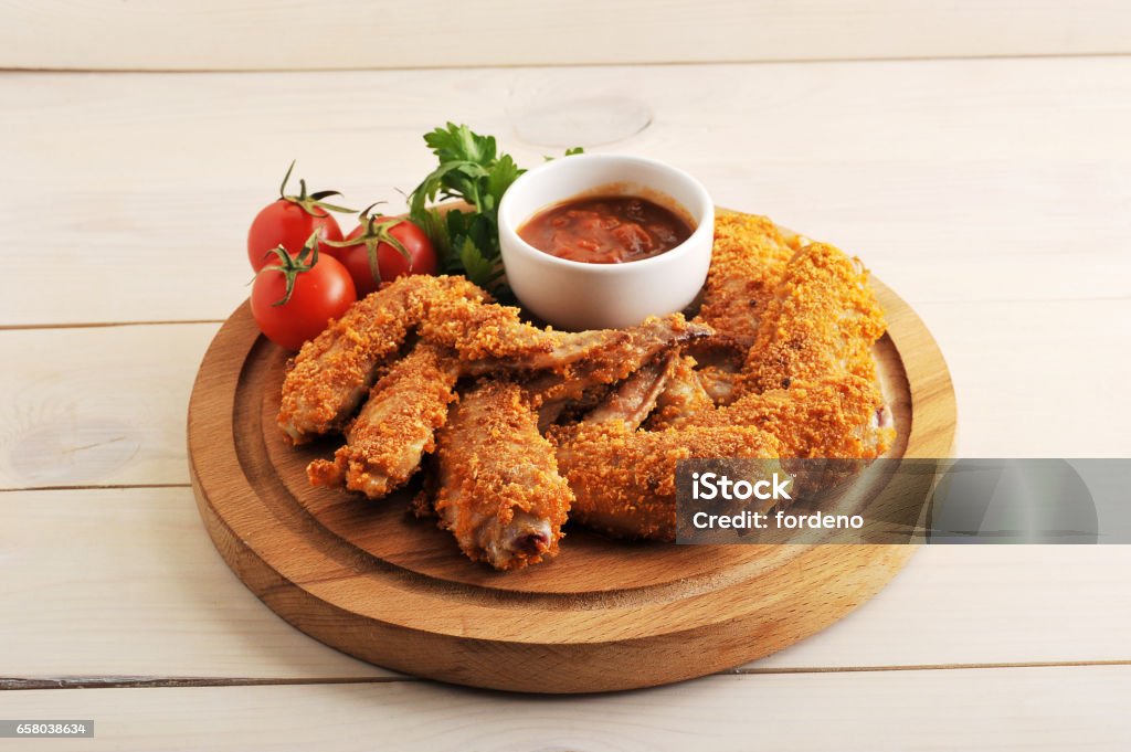 fried chicken wings breaded with ketchup, tomato and parsley on a circular wooden Board