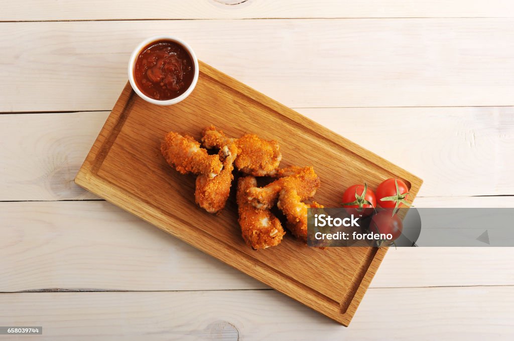 fried chicken in breadcrumbs with ketchup, tomatoes on a rectangular wooden Board - top view