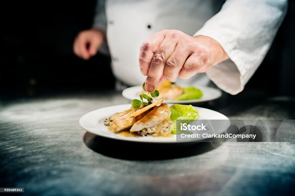 Professional chef putting the final flourish to the dish by adding a sprig of watercress to the dish of slow cooked chicken breast served on a bed of bulgur risotto. Colour, horizontal with some copy space. Photographed in a restaurant on the island of Møn in Denmark.